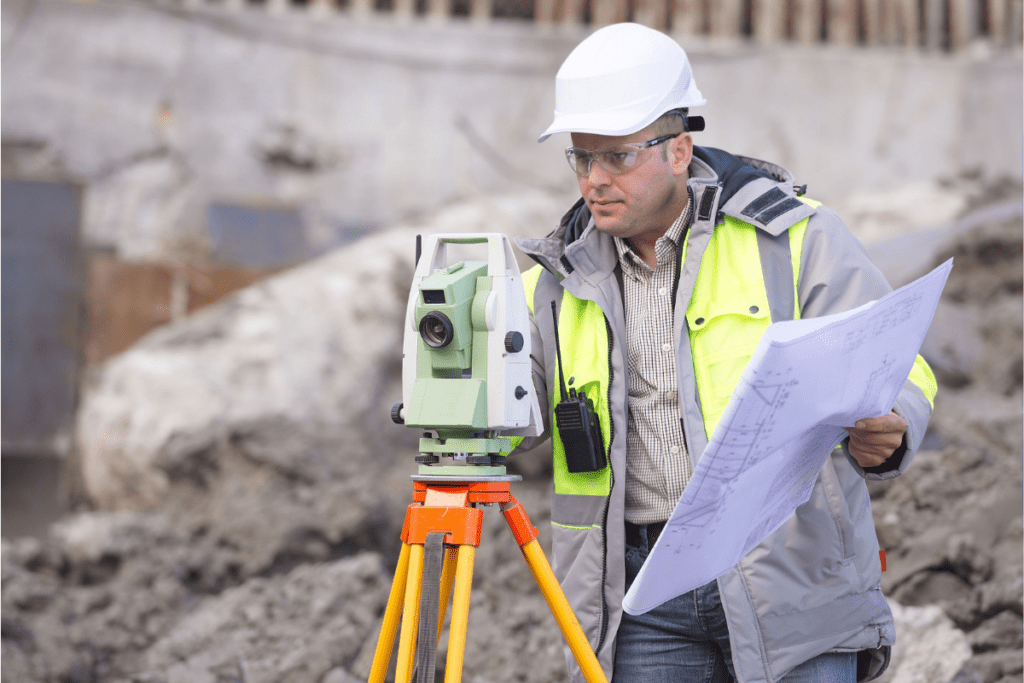 A Man Wearing A Hard Hat Uses A Theodolite To Survey A Building Site To Earn His Land Surveyor'S Salary In Canada