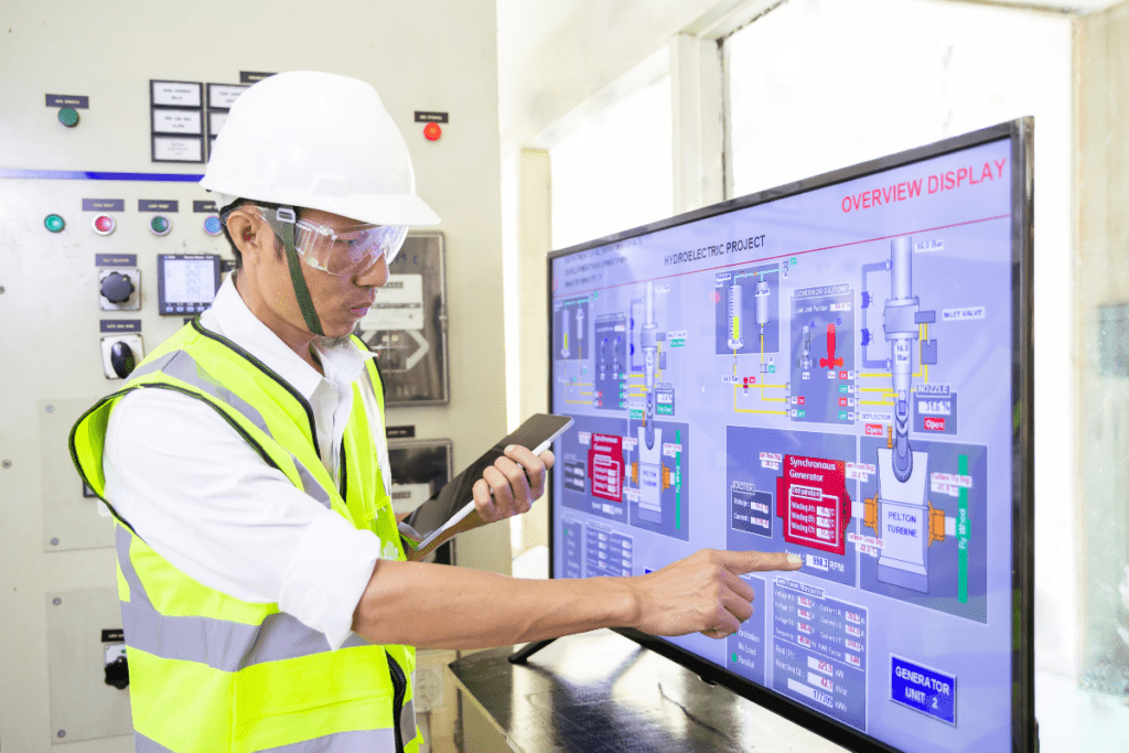 Un travailleur portant un gilet fluorescent jaune et un casque de sécurité examine la conception d'un circuit sur un grand écran pour le salaire d'un ingénieur électricien au Canada
