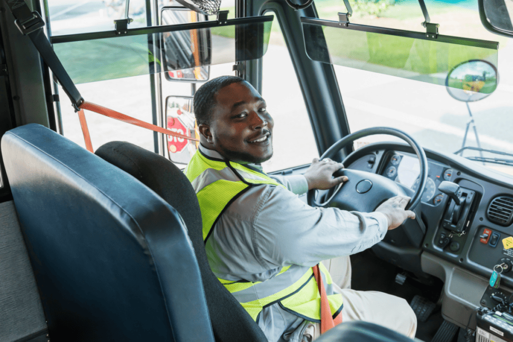 Un chauffeur de bus souriant portant un gilet jaune fluorescent est assis dans sa cabine pour connaître le salaire du chauffeur de bus au Canada