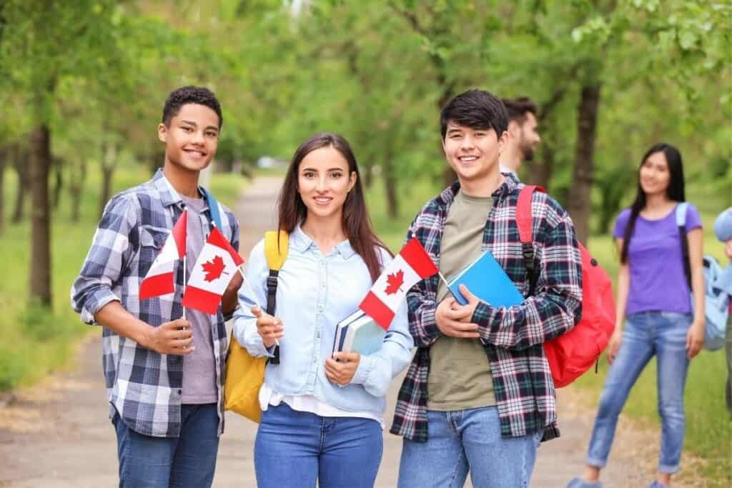 Three Young Immigrants Of Canada Stand In A Park Holding Canadian Flags Provincial Nominee Program One Of The Best Reasons To Move To Manitoba